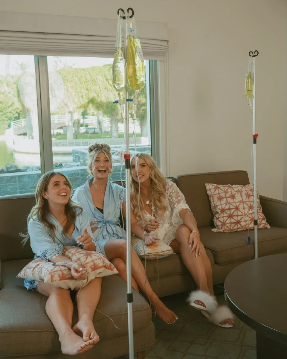 Friends in matching robes laughing on a sofa, each with an IV