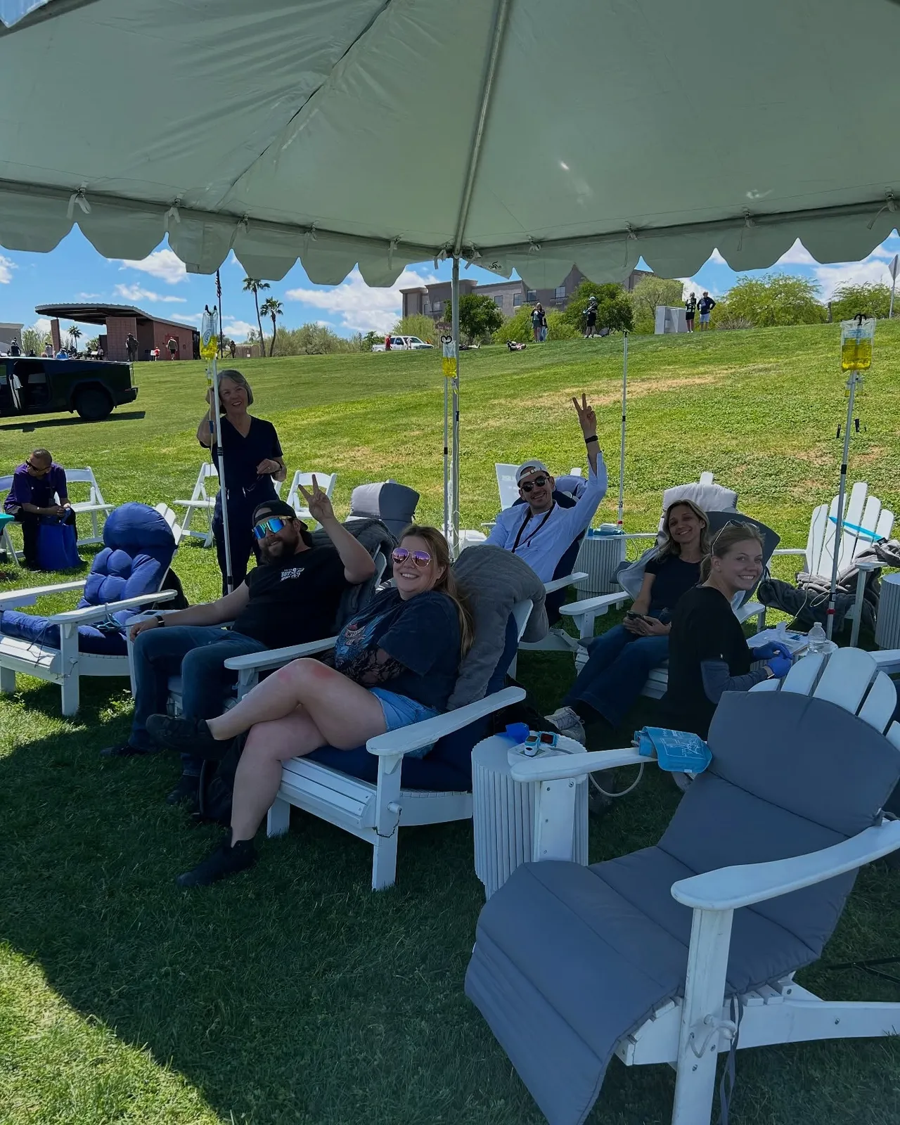 Guests in lawn chairs with their IVs under a white tent on the grass
