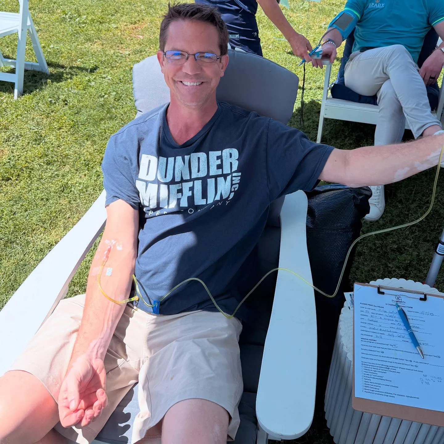 A smiling guest with his IV in a chair on the grass on a sunny day